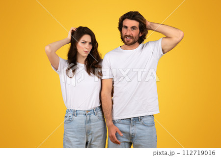Perplexed young couple in white t-shirts and jeans, scratching their heads with puzzled expressions 112719016