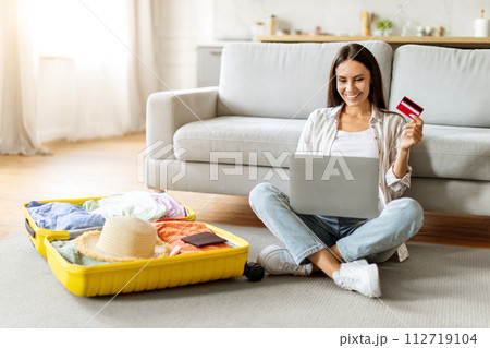 Smiling european woman using her laptop and credit card to book trip Smiling european woman using her laptop and credit card to book trip 112719104