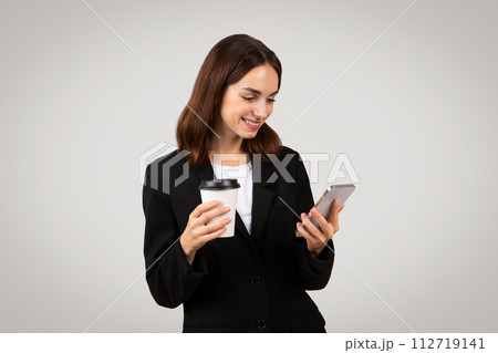 Multitasking businesswoman in a smart black suit happily checks her smartphone Multitasking businesswoman in a smart black suit happily checks her smartphone 112719141