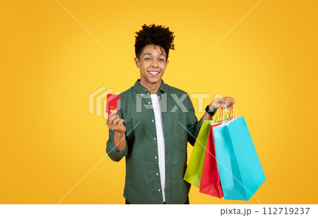 Positive african american guy showing credit card and purchases Positive african american guy showing credit card and purchases 112719237