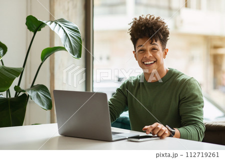 Cheerful millennial black man freelancer working at cozy cafe 112719261