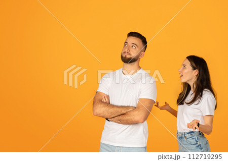 Skeptical man with crossed arms looking unconvinced beside a talking woman Skeptical man with crossed arms looking unconvinced beside a talking woman 112719295