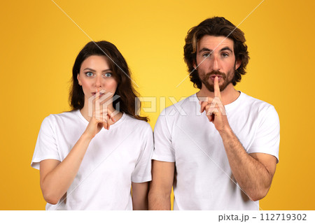 A young woman and a man with dark hair and white t-shirts gesture for silence 112719302