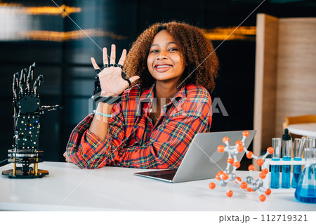 Black teenage student in a classroom learns and tests a robotic arm on a table delving into subjects of interest. Embracing innovation and technology for skill development in education. Black teenage student in a classroom learns and tests a robotic arm on a table delving into subjects of interest. Embracing innovation and technology for skill development in education. 112719321