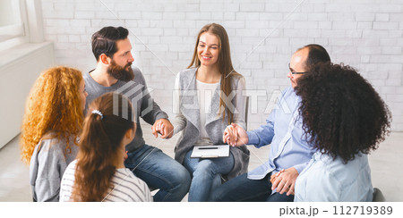 Diverse people sitting on chairs in circle holding hands 112719389