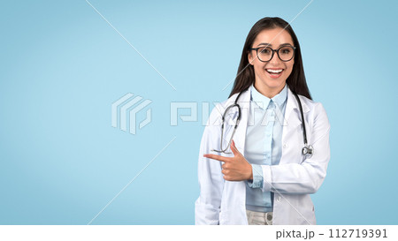 Happy female doctor with glasses pointing at free space on blue 112719391