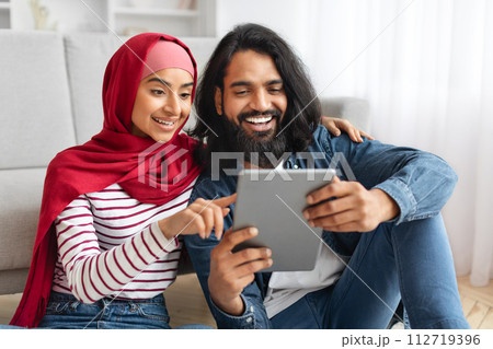 Smiling muslim couple with digital tablet relaxing on floor at home 112719396