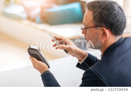 A mature businessman in a smart suit uses contactless payment with his smartphone 112719459