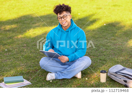Brazilian student guy browsing internet on digital tablet learning outside 112719468