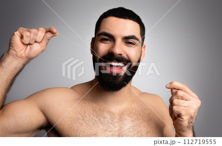 Positive half-naked middle eastern bearded man using dental floss Positive half-naked middle eastern bearded man using dental floss 112719555