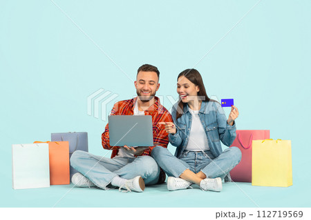 Couple Using Credit Card And Laptop Shopping Over Blue Backdrop Couple Using Credit Card And Laptop Shopping Over Blue Backdrop 112719569