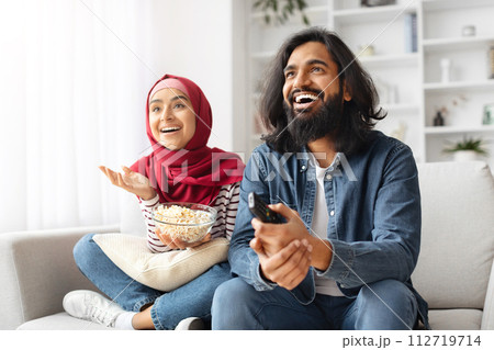 Cheerful muslim couple enjoying funny movie on TV while relaxing at home 112719714