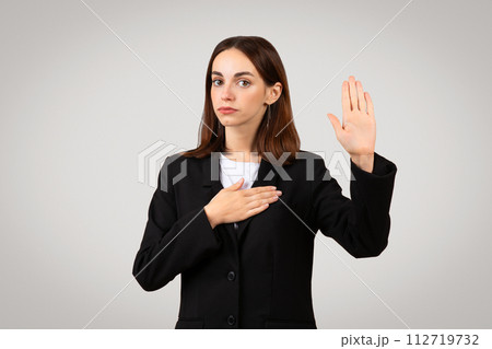 Solemn businesswoman in a black suit takes an oath with her right hand raised Solemn businesswoman in a black suit takes an oath with her right hand raised 112719732