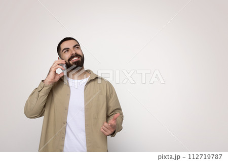 Confident young man with a full beard engaging in a pleasant conversation on a mobile phone Confident young man with a full beard engaging in a pleasant conversation on a mobile phone 112719787