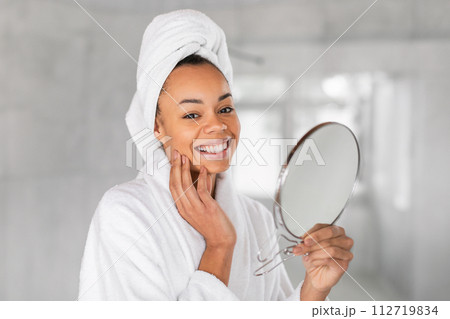black lady holds round mirror touches face, portrait in bathroom 112719834