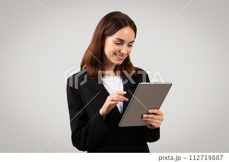 An attentive young businesswoman in a black blazer is focused on a tablet she's holding An attentive young businesswoman in a black blazer is focused on a tablet she's holding 112719887