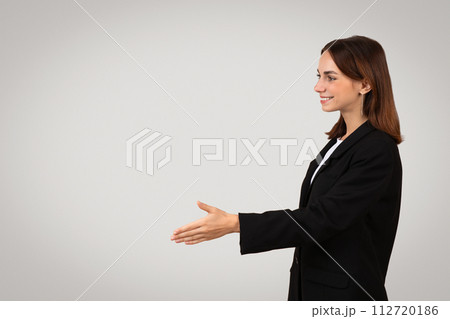 Side profile of a smiling young businesswoman in a black suit extending a handshake 112720186