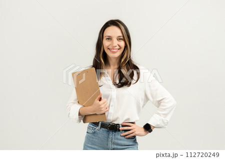 Smiling young professional woman holding a clipboard, wearing a white blouse 112720249