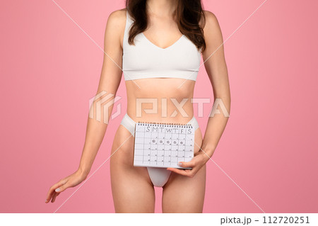 A woman in white fitness attire confidently holds a calendar near her waist 112720251