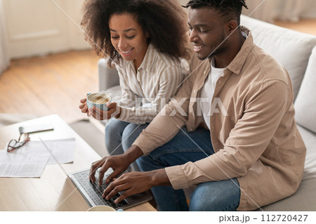 Black couple engaged with paperwork and laptop in living room Black couple engaged with paperwork and laptop in living room 112720427