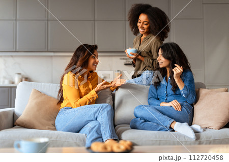 Multiethnic women share stories sitting with cups of tea indoors 112720458