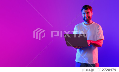 Young caucasian guy using laptop in studio with neon light 112720479