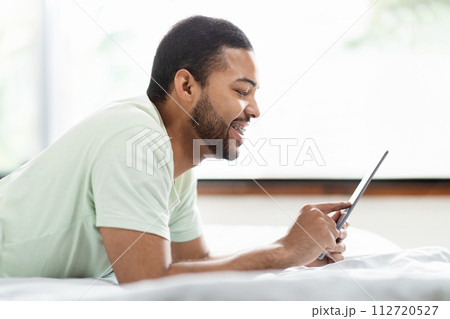 African american man using tablet in bed, using mobile app African american man using tablet in bed, using mobile app 112720527
