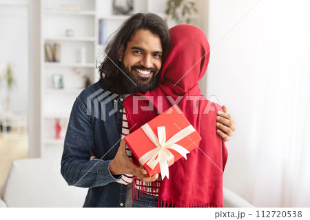 Happy Arab Man Embracing His Muslim Wife And Holding Gift Happy Arab Man Embracing His Muslim Wife And Holding Gift 112720538