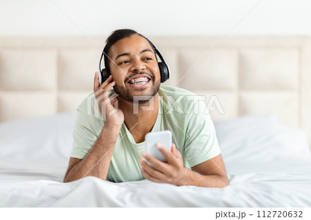Positive african american guy listening to music in bedroom 112720632