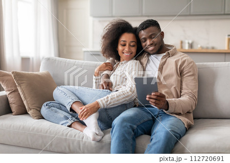 Happy black husband and wife enjoying movie on tablet indoor 112720691