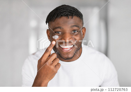 Headshot of joyful African man applies facial moisturizer on cheek Headshot of joyful African man applies facial moisturizer on cheek 112720763