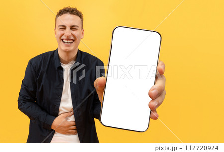 Happy young guy showing phone and laughing Happy young guy showing phone and laughing 112720924