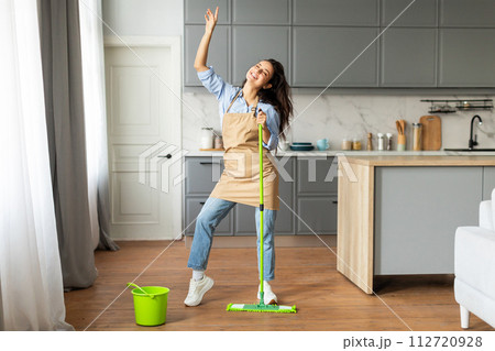 Happy woman dancing while mopping the floor in modern kitchen Happy woman dancing while mopping the floor in modern kitchen 112720928