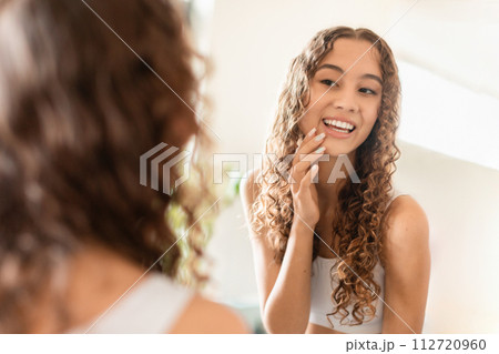 teenager girl touches smooth skin looking in the mirror indoor 112720960