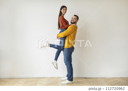 Happy young man joyfully lifting his smiling girlfriend at home Happy young man joyfully lifting his smiling girlfriend at home 112720962