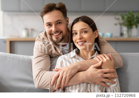 Happy couple embracing on the sofa and smiling at camera 112720968