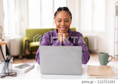 Cheerful black lady student with laptop in purple shirt, studying at home Cheerful black lady student with laptop in purple shirt, studying at home 112721283