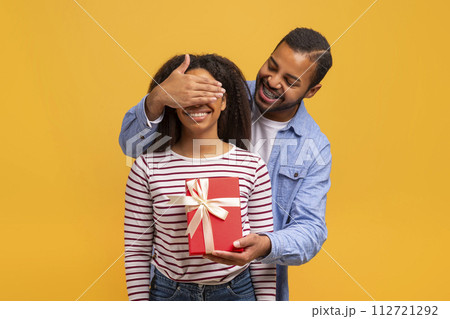 Surprise Concept. Romantic black man covering his girlfriend's eyes and giving gift 112721292