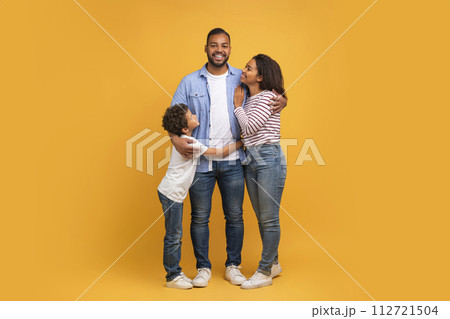Family Warmth. African American Father, Mother And Son Embracing Against Yellow Background Family Warmth. African American Father, Mother And Son Embracing Against Yellow Background 112721504