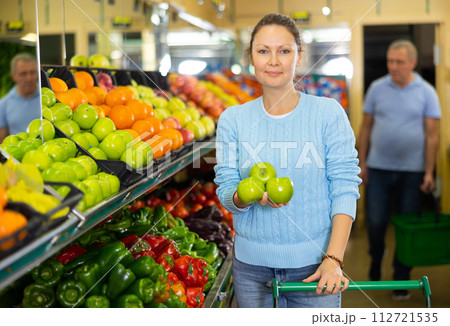 Positive middle-aged female buyer choosing organic granny smith green apples in hypermarket 112721535