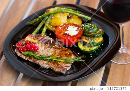 Fried beef loin with vegetables and red currant on wooden background Fried beef loin with vegetables and red currant on wooden background 112721573