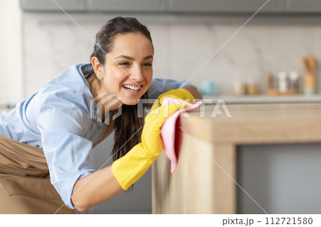 Smiling woman dusting furniture in the kitchen, copy space 112721580
