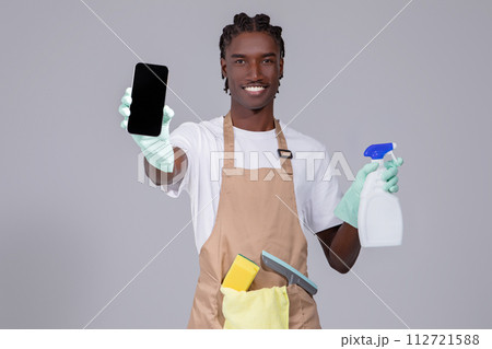 Cleaning Service Ad. Black Man Wearing Apron Showing Blank Smartphone In Hand 112721588