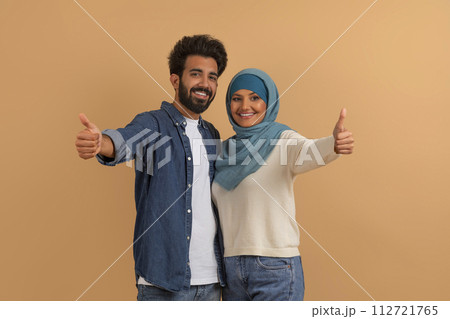 Arabic Couple, Man And Woman In Hijab Showing Thumbs Up At Camera Arabic Couple, Man And Woman In Hijab Showing Thumbs Up At Camera 112721765