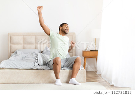 Happy well-rested black man stretching in bed Happy well-rested black man stretching in bed 112721813