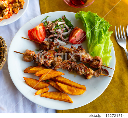 Lamb shish kebab with lettuce, tomatoes and French fries closeup. Turkish cuisine Lamb shish kebab with lettuce, tomatoes and French fries closeup. Turkish cuisine 112721814