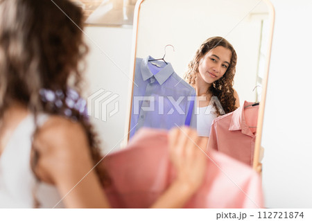 teen lady near mirror holding shirts making fashion choices indoor 112721874