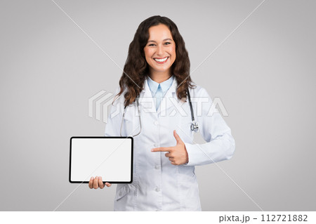 Friendly female doctor presenting digital tablet with blank screen, ideal for displaying health apps or medical ad 112721882