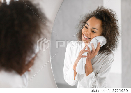 Happy black lady wiping face with towel in modern bathroom Happy black lady wiping face with towel in modern bathroom 112721920