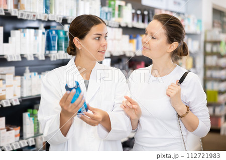 Female buyer consults the pharmacist which lotion or ointment to buy at pharmacy 112721983